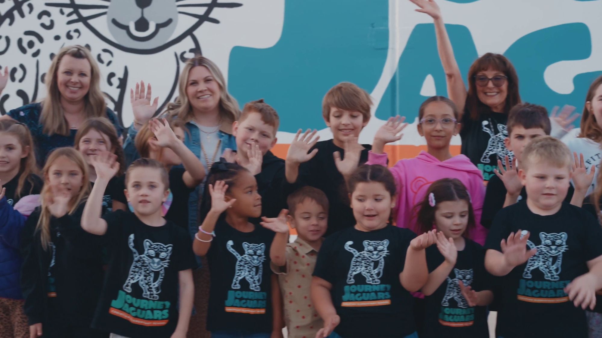 Journey Christian School students and teachers waving in front of the Journey Jaguars mural